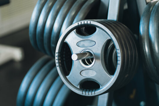 Dumbbell, weight plate, and barbell in dark gym create focused strength training scene with metallic texture and athletic equipment detail