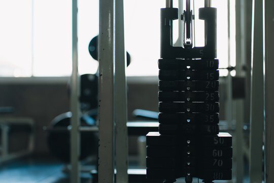 Weight plate cable machine gym equipment strength training setup with dark metal plates and blurred workout space, creating focused athletic atmosphere for fitness exercise