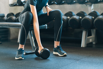 Woman lifting dumbbell in gym during strength training workout with focused energy, seated on bench...