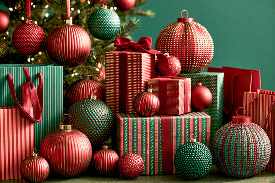 A rich stack of red and green Christmas gift boxes and shopping bags beautifully surrounded by textured holiday baubles near a decorated pine tree