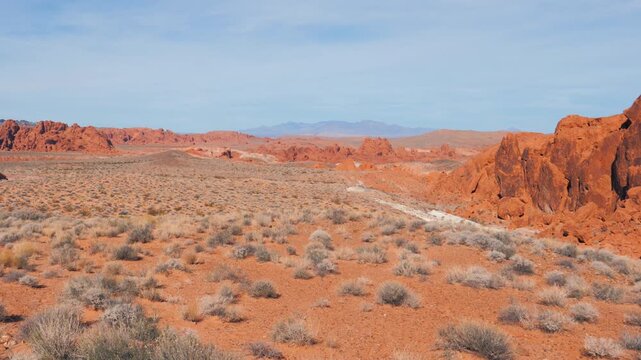 Expansive desert landscape featuring iconic red sandstone formations, dry bushes and distant mountains under a clear blue sky in valley of fire state park, nevada, showcasing the arid beauty