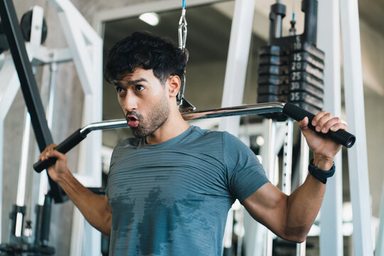 Muscular man performing lat pulldown exercise in modern gym with focused expression and strength training equipment