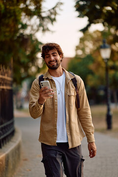 Happy man using smart phone app while walking on street.