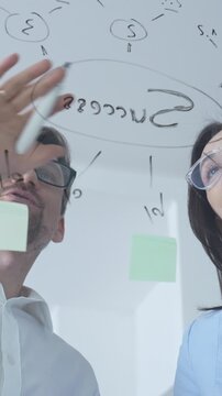 Business colleagues collaborating on an innovative project, brainstorming ideas and developing a strategic plan using sticky notes on a clear glass whiteboard