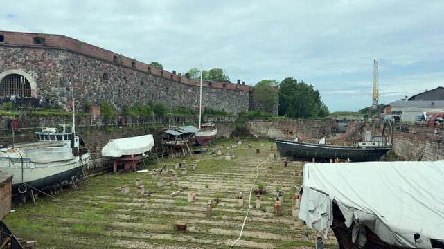 Wide view of the historic dry dock at Suomenlinna sea fortress with traditional wooden vessels undergoing restoration inside the stone basin in Helsinki, Finland.