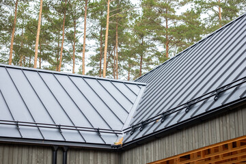 Obraz premium Modern metal standing seam roof of house near pine trees includes snow guards and gutters on wooden residential architecture.