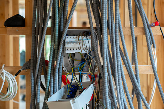 Electrical panel installation with corrugated conduits on wooden frame during residential house construction, showing circuit breakers, cabling, and conduits.