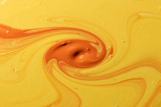 Yellow and orange paint swirl mixing in abstract liquid background. Colorful fluid art pattern with vortex motion. Creative texture backdrop for decoration and design concept