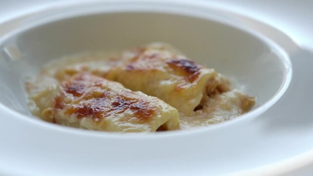 Baked chicken cannelloni with melted cheese and creamy bechamel sauce served on a white plate