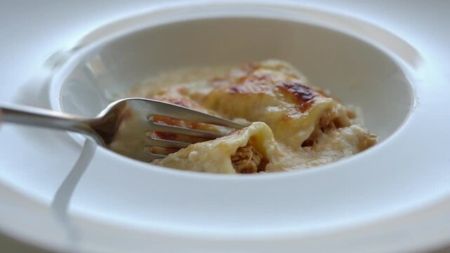 Close-up of fork touching fresh baked chicken cannelloni with bechamel sauce
