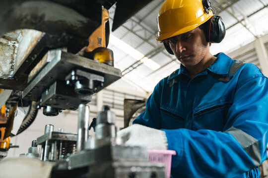 Industrial worker in blue coverall and safety helmet operating heavy machinery inside factory, focused on precision manufacturing and workplace safety