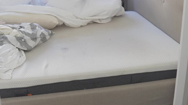 Woman removing used and dirty bed linen from a mattress in a bedroom. Changing sheets and preparing the bed for fresh bedding during household cleaning