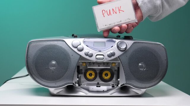 Hand inserting a retro punk cassette into a vintage boombox, close up evoking 80s90s analog audio nostalgia, diy music culture and portable stereo listening memories