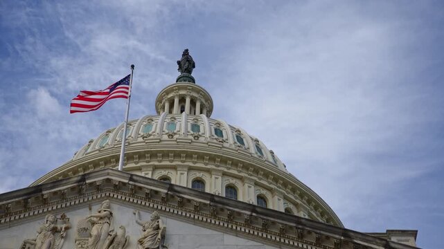 American flag moving in wind on Capitol. American flag with clouds over US Capitol. American flag strong symbol of Amerika freedom. American flag on landmark Capitol dome in Washington DC.