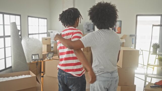 Two men hug with arm around shoulder beside stacked moving boxes and tools in a sunlit building; hope friendship.