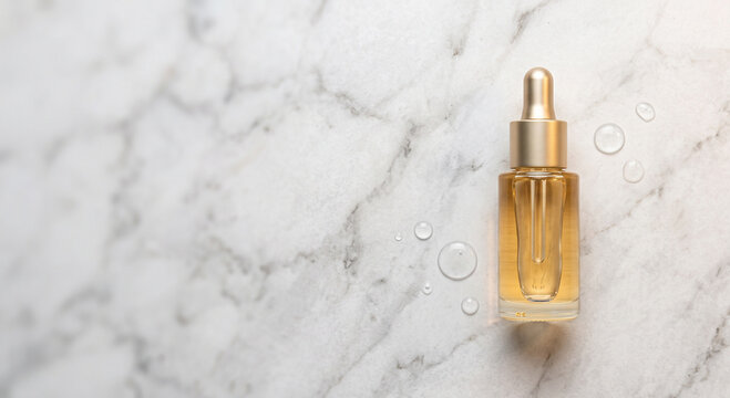 Golden oil cosmetic serum dropper bottle mockup on a white marble background with water drops and copy space.