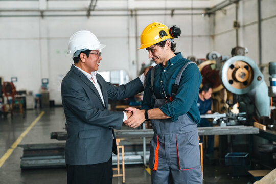 Industrial engineer greeting factory worker inside manufacturing workshop, sharing handshake and friendly smile during workplace collaboration and safety training
