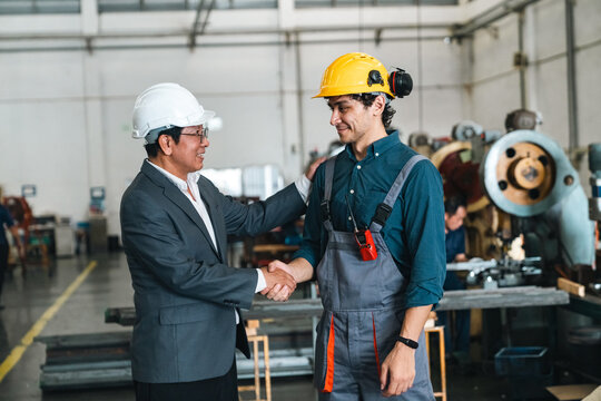 Industrial manager and factory worker shaking hands during workplace collaboration with machinery in background, expressing trust and professional teamwork