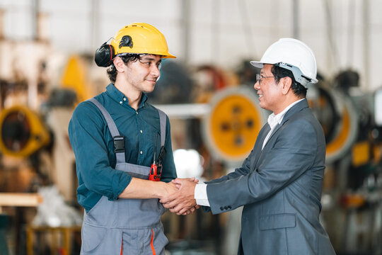 Young industrial worker and senior manager shaking hands inside manufacturing factory, expressing trust, cooperation, and professional partnership