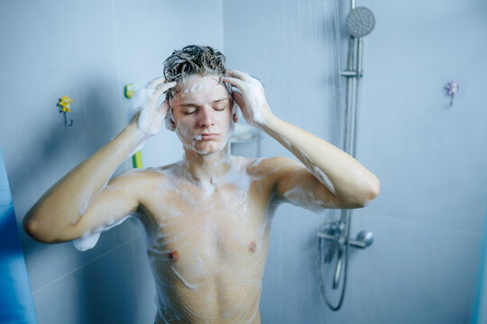 Sleepy teenager massaging shampoo into his wet hair during morning shower.