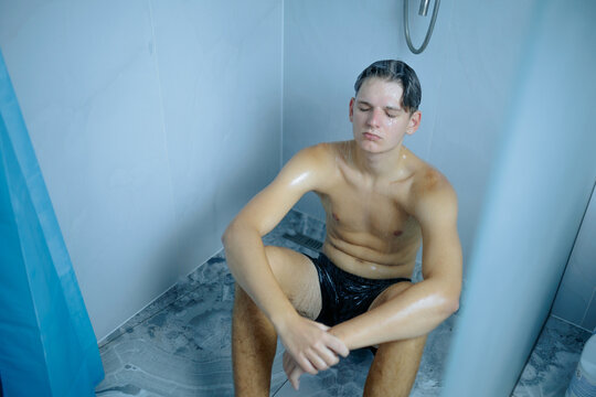 Upset adolescent male hugging his knees on the bathroom floor.