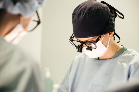 Young female surgeon performing a cardiac operation in a sterile operating room, carefully working at the operative field while using surgical loupes and maintaining precision throughout the procedure