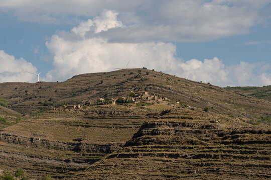 Distant view of abandoned ghost village ruins on terraced mountain with wind turbines
