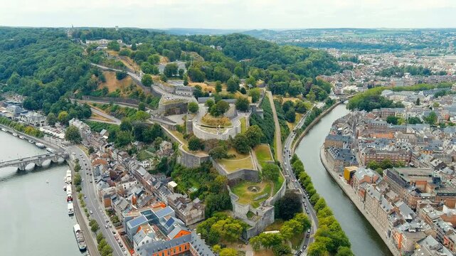 Namur, Belgium. Citadelle de Namur, a sprawling stone fortress with layered ramparts and grassy terraces, aerial panoramic view over the Meuse River on a bright summer day. Drone footage