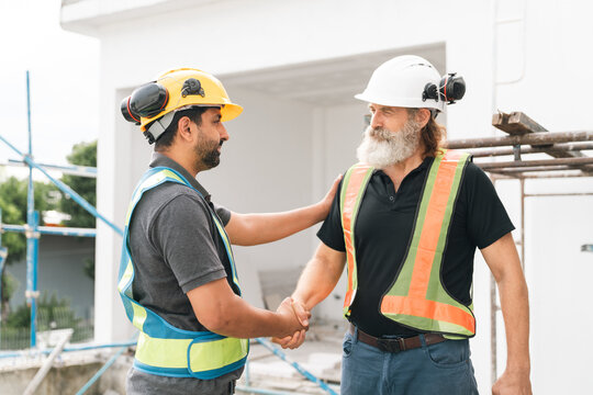 Construction worker handshake at building site with diverse male colleagues, safety helmet, reflective vest, trust and teamwork