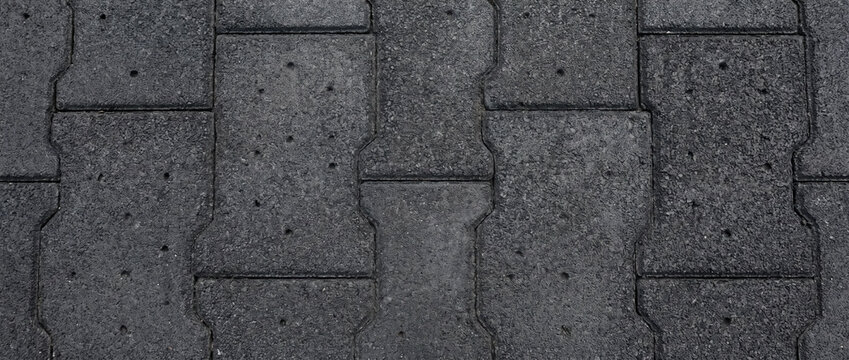 Dark grey rubber pavement texture with interlocking block pattern and small holes. Rubber tile surface