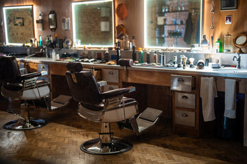 Obraz premium Cozy interior of barbershop with classic vintage chairs, illuminated mirrors and professional grooming tools arranged on counters for clients, indoor setting of hair salon with stylish furniture.