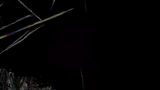 Real time 10x microscope macro of explosive crystal growth with sharp silver, gold and blue needle structures gradually expanding to completely fill the deep black cross polarization background