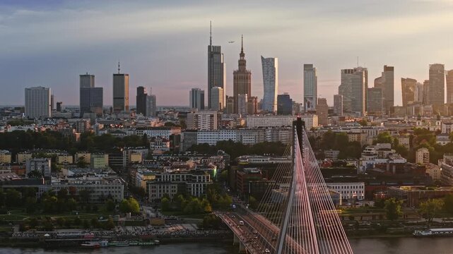 Smooth aerial panorama from left to right across Warsaw at golden hour, revealing Swietokrzyski Bridge over the Vistula River and downtown skyline with modern skyscrapers in warm evening light