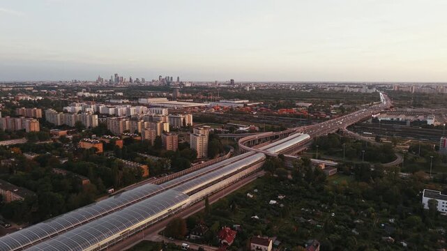 Wide aerial drone panorama over city at golden hour, revealing S8 expressway, acoustic tunnels, residential districts and distant downtown skyline