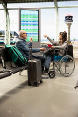 Senior man supporting woman in wheelchair at airport
