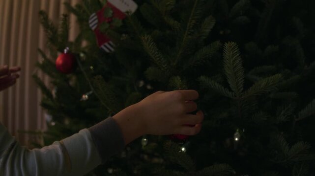 Young boy hanging up christmas decorations on indoor christmas tree gets pricked by real tree bristle