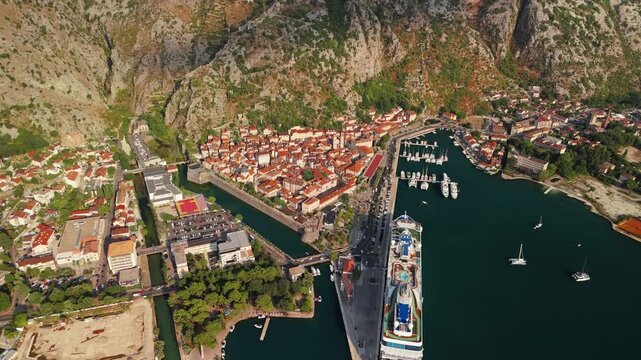 aerial pull back showing the small old town and marina of kotor dwarfed by a huge rocky amphitheatre of bare cliffs and gullies behind, bay of kotor, montenegro