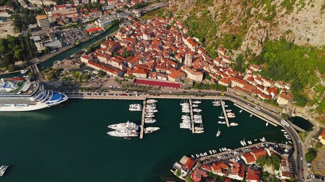 kotor, montenegro - aerial establishing shot of kotor old town in summer, a walled medieval town with red tile roofs, a yacht marina and a cruise ship at the quay below steep mountains
