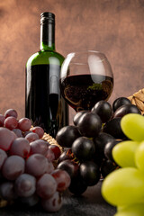 Fototapeta premium Arrangement of grapes and a bottle of red wine; beautiful grapes, a bottle of red wine, and accessories on a stone surface; abstract background, selective focus.