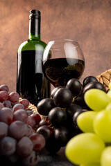Fototapeta premium Arrangement of grapes and a bottle of red wine; beautiful grapes, a bottle of red wine, and accessories on a stone surface; abstract background, selective focus.