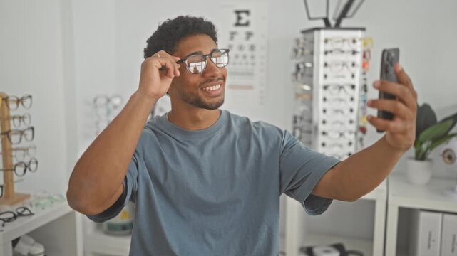 Man adjusts eyeglasses on face while holding smartphone and smiling during fitting in optician studio; confidence connection.