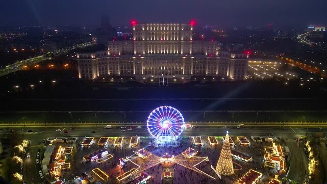 Aerial drone footage of the festive Bucharest Christmas Market illuminated at night in Constitution Square (Piata Constitutiei), featuring the glowing Ferris wheel, decorated Christmas tree.