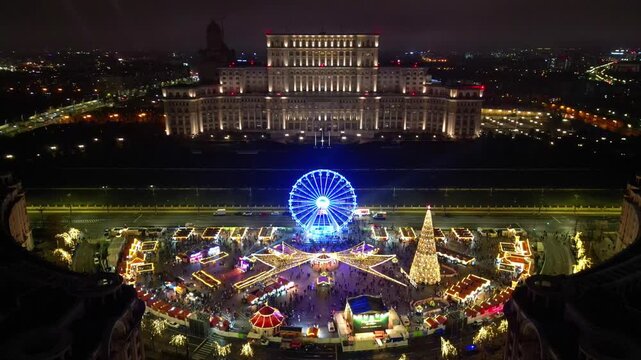 Aerial drone footage of the festive Bucharest Christmas Market illuminated at night in Constitution Square (Piata Constitutiei), featuring the glowing Ferris wheel, decorated Christmas tree.