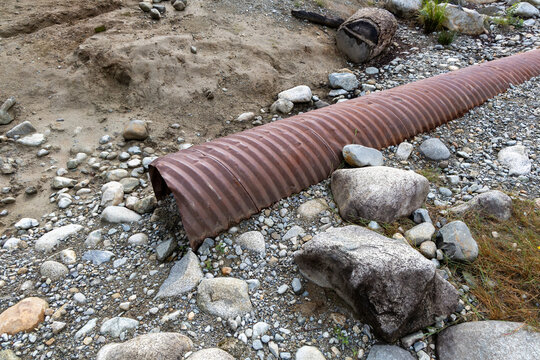 Rusty Corrugated Drainage Pipe on Rocky Dry Riverbed Landscape Showing Erosion in BC, Canada