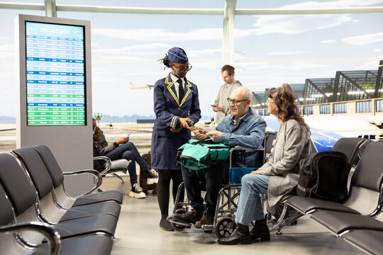 African American cabin crew member assists an older wheelchair user at the gate, checking a boarding pass and travel documents while explaining departure time.