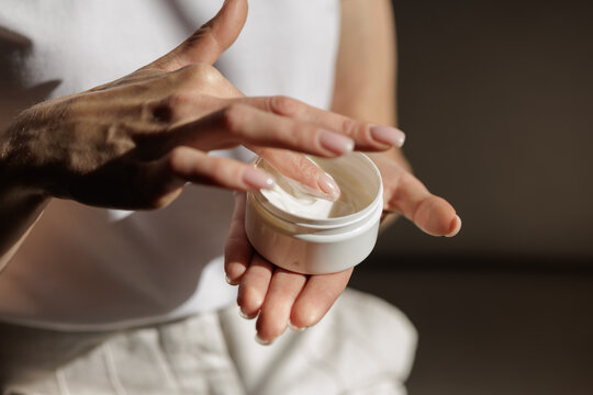 Mature Woman Scooping Facial Moisturizer During Sunlit Morning Skincare Routine