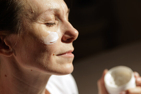 Mature Woman Applying Face Cream in Warm Morning Sunlight
