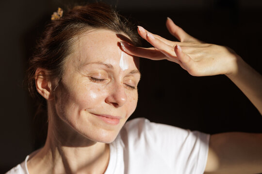 Mature Woman Applying Facial Moisturizer in Warm Morning Sunlight