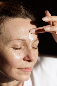 Mature Woman Applying Face Cream During Sunlit Skincare Routine