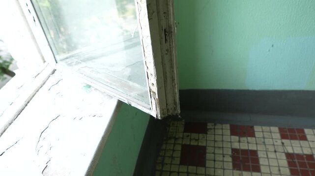 Interior view of an empty neglected room with an open window, worn floor and outdated apartment condition, representing abandoned property, renovation, housing problems and real estate restoration con